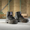 Pair of black work boots on a concrete floor with a metal staircase in the background