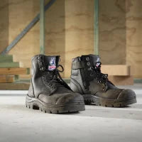 Pair of black work boots on a concrete floor with a metal staircase in the background