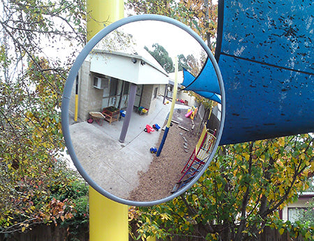 Outdoor convex mirror mounted on a pole overlooking a childcare playground